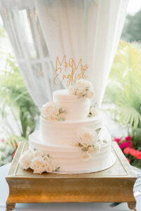 three-tiered white wedding cake with flowers and personalized cake topper
