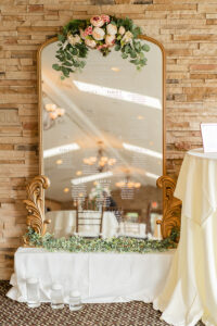 Wedding seating assignments on gold mirror adorned with flowers